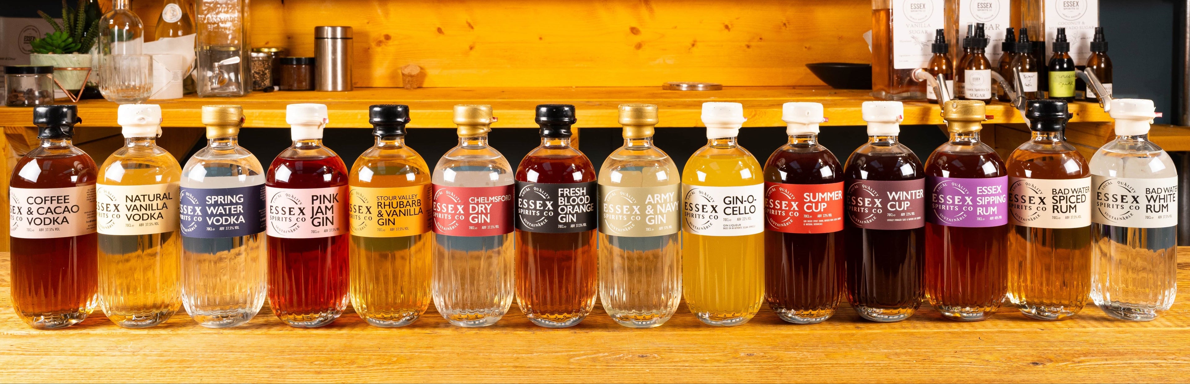Row of various bottles on a bar counter with a wooden shelf in the background.