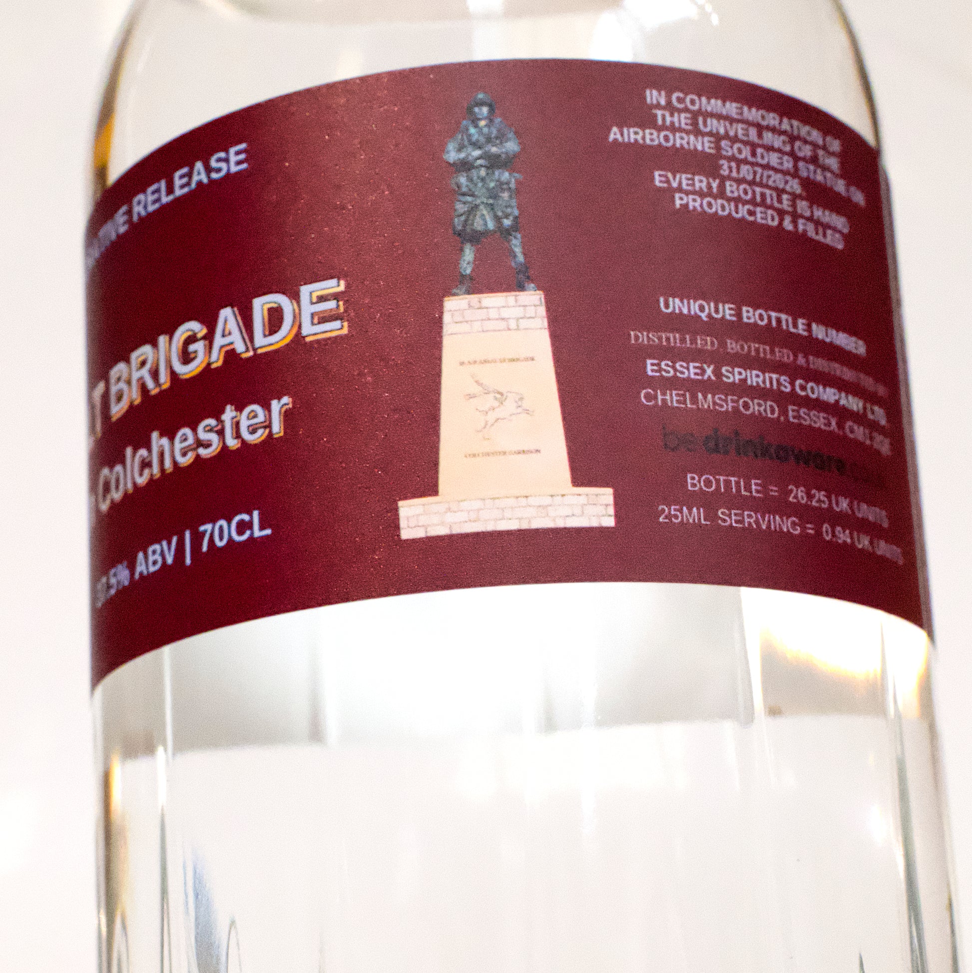Close-up of a bottle label for 'Brigade Colchester' ABV 18% from Essex Spirits Company, featuring a dark red background with white and gold text and a statue illustration.