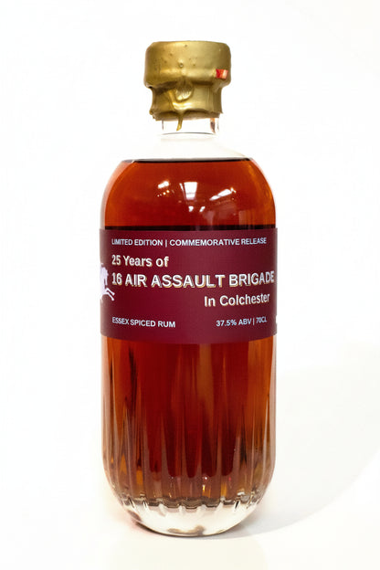 A bottle of commemorative Essex Spiced Rum with amber liquid, a gold cap, and a dark red label reading '25 Years of 10th Air Assault Brigade in Colchester'.
