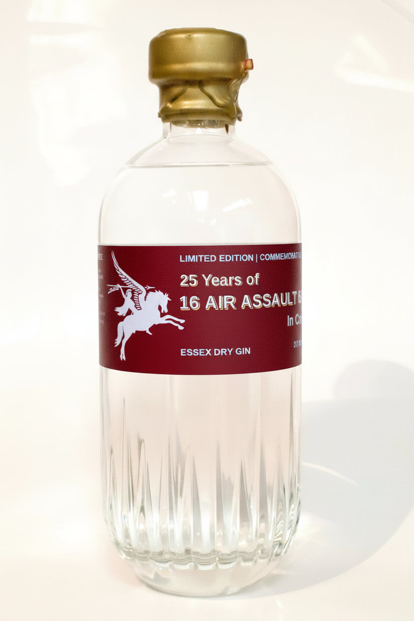 A clear glass bottle of Essex Dry Gin with a gold cap and a dark red label featuring a white winged horse graphic and text reading '25 Years of 16 Air Assault' and 'Essex Dry Gin'.