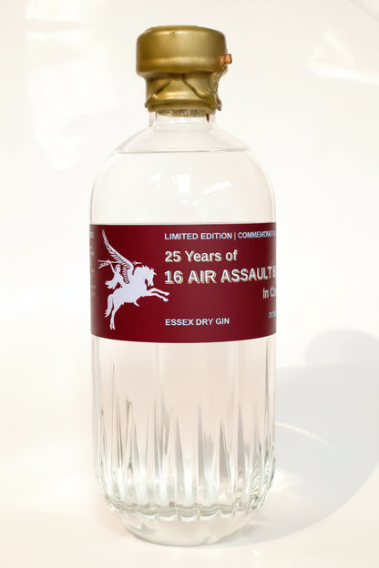 A clear glass bottle of Essex Dry Gin with a gold cap and a dark red label featuring a white winged horse graphic and text reading '25 Years of 16 Air Assault' and 'Essex Dry Gin'.