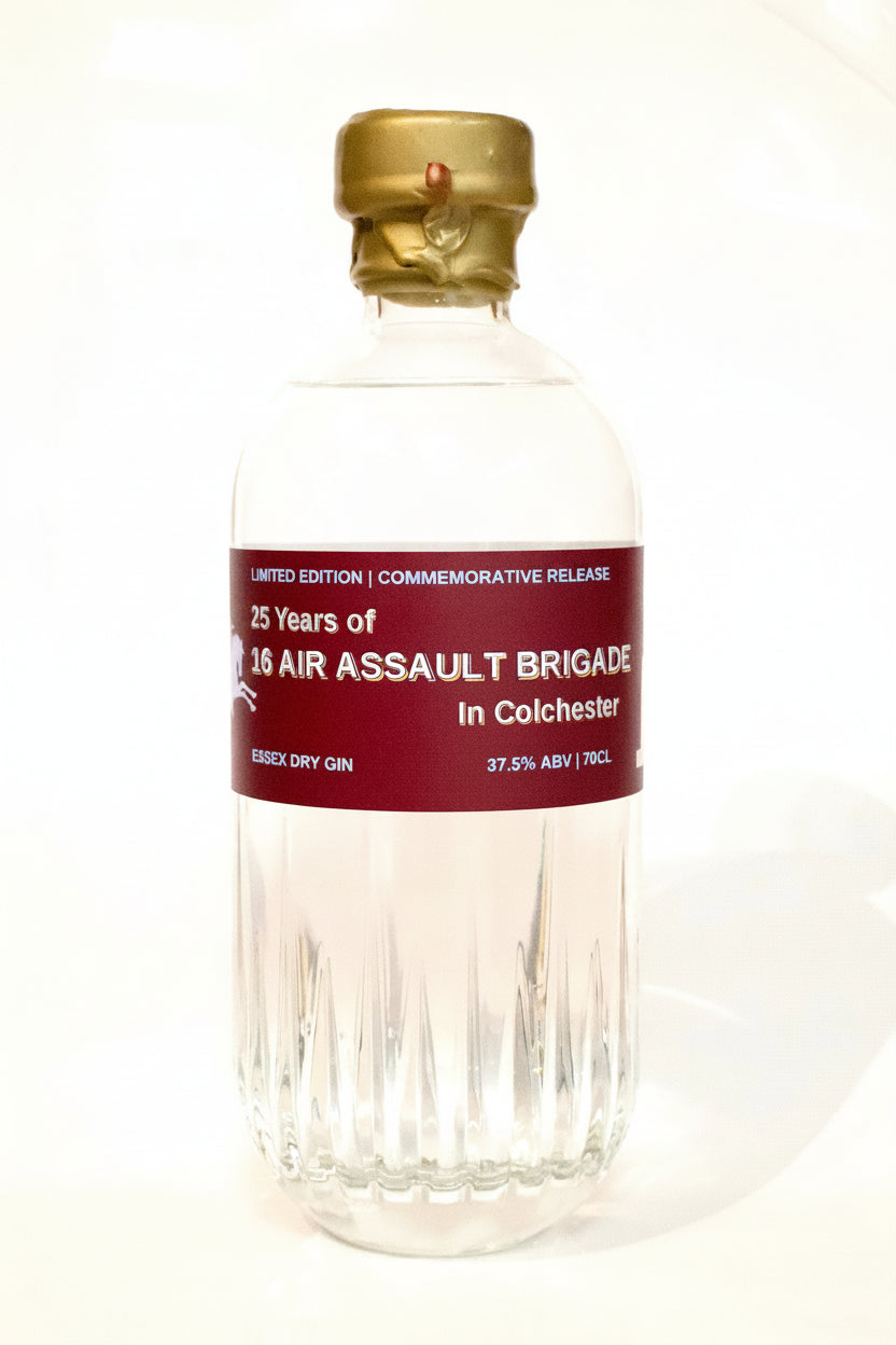A clear glass bottle of Colchester 25 Years of 16 Air Assault Brigade Essex Spirits Co. Dry Gin with a gold cap and a dark red label, set against a plain white background.