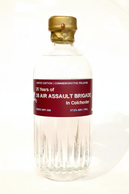A clear glass bottle of Colchester 25 Years of 16 Air Assault Brigade Essex Spirits Co. Dry Gin with a gold cap and a dark red label, set against a plain white background.
