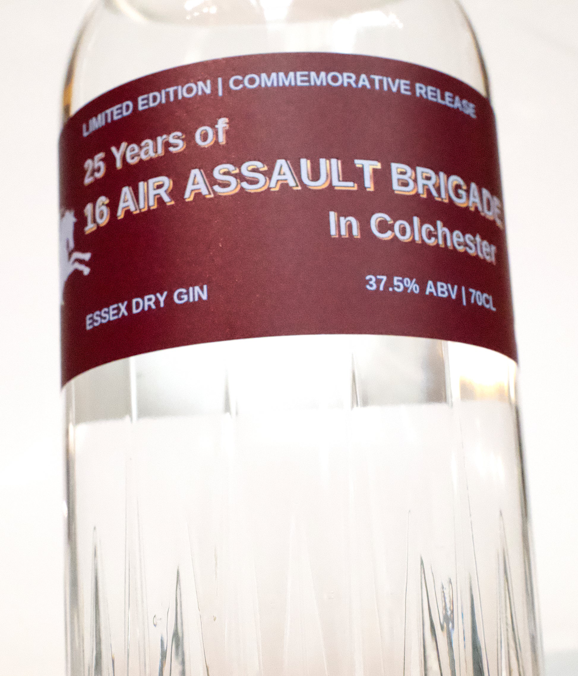 A close-up of a clear glass bottle of Essex Dry Gin with a dark burgundy label reading '25 Years of 16 Air Assault Brigade in Colchester' and 'Limited Edition Commemorative Release'.