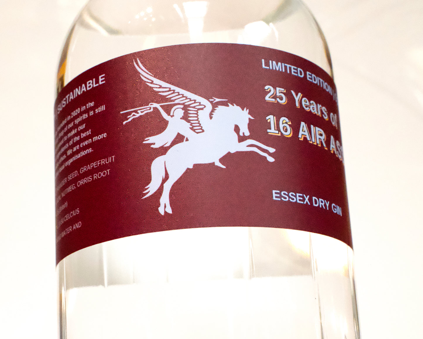 A close-up of a clear glass bottle of 16 Air Asa 25 Years Limited Edition Essex Dry Gin, featuring a dark maroon label with a white Pegasus graphic and white text.