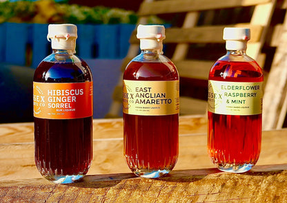 Three bottles of different types of liquor on a wooden surface with a blurred outdoor background.