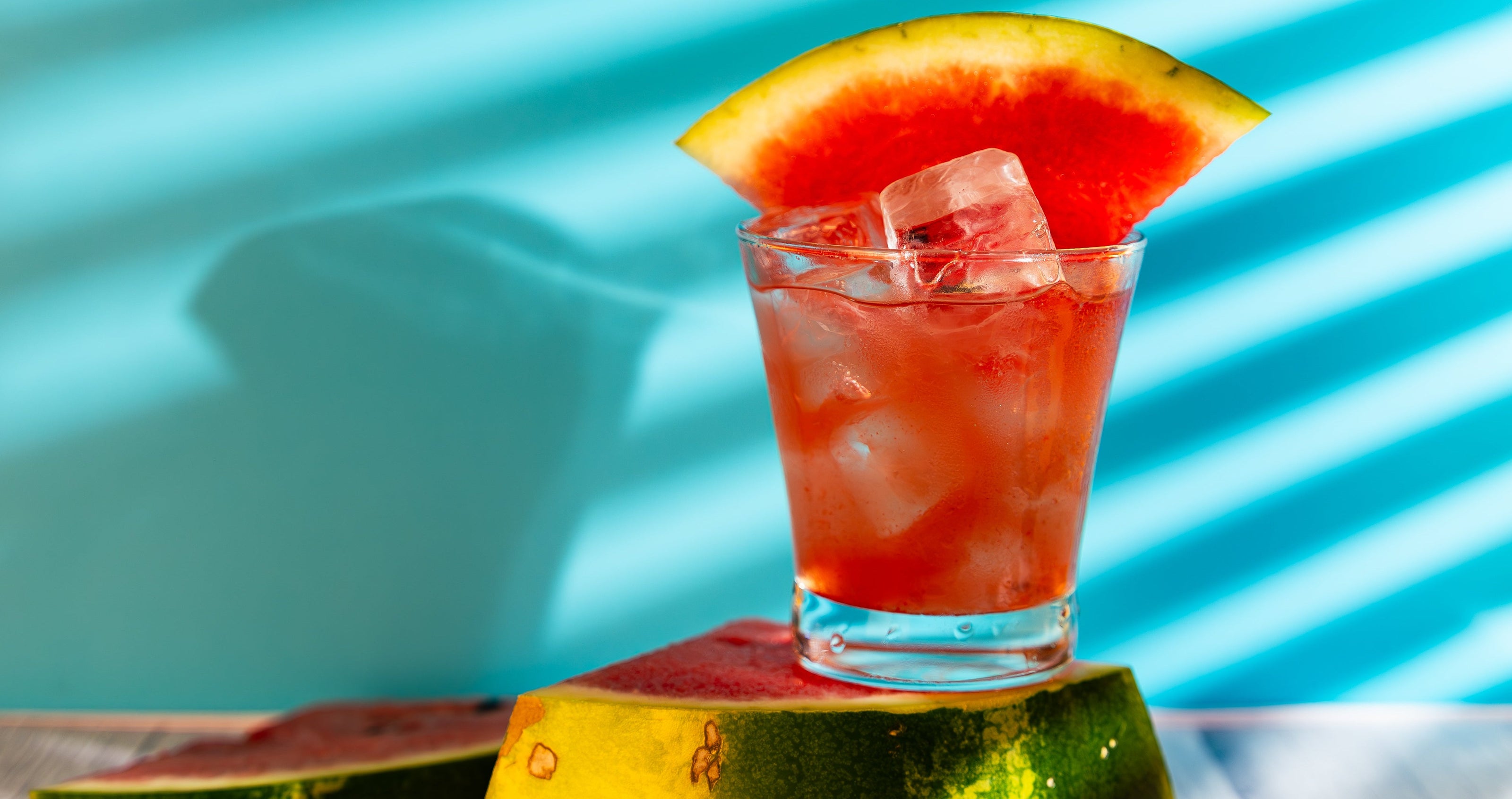 Cocktail with ice and watermelon slice on a watermelon base against a blue background
