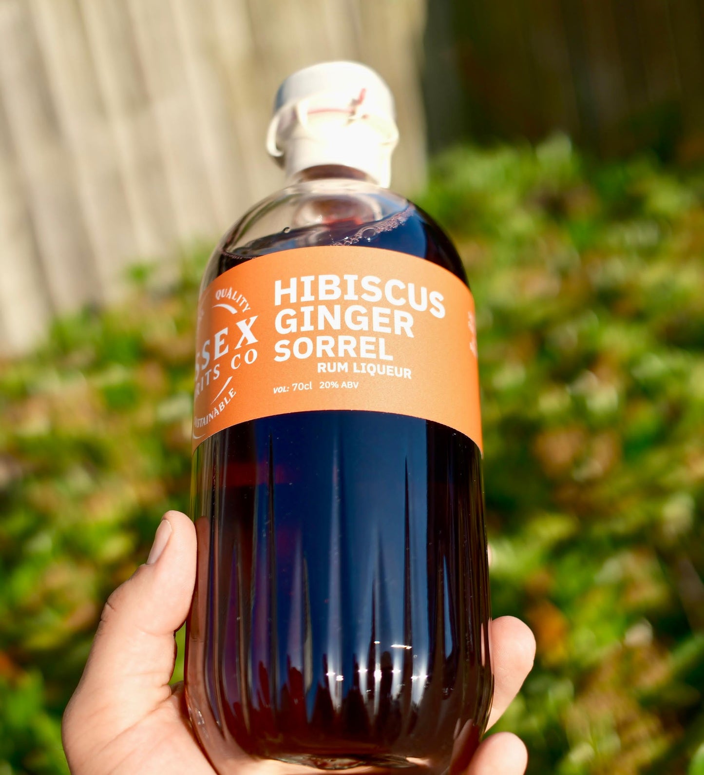Bottle of Essex & Co. Hibiscus Ginger Sorrel Rum Liqueur held in a hand with a blurred green background