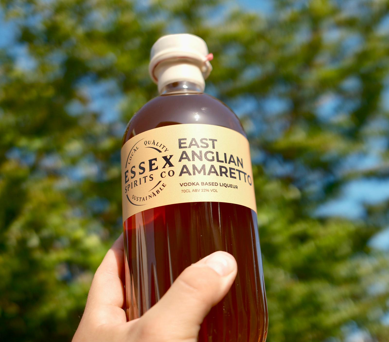 Bottle of East Essex Anglian Spirits Co Amaretto held in a hand with a blurred green and blue background