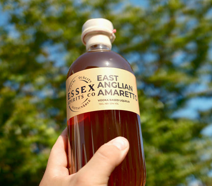 Bottle of East Essex Anglian Spirits Co Amaretto held in a hand with a blurred green and blue background